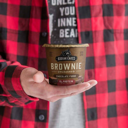 Person holding Kodiak Cakes Chocolate Fudge Brownie Cake Cup, a high-protein snack with real chocolate fudge and whole grains.